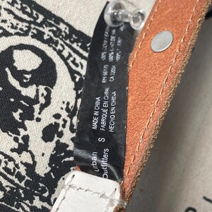 May include: Close-up of a brown and white leather belt with a silver buckle. The belt has a small tag that reads "Urban Outfitters" and "MADE IN CHINA". The belt is a size small.