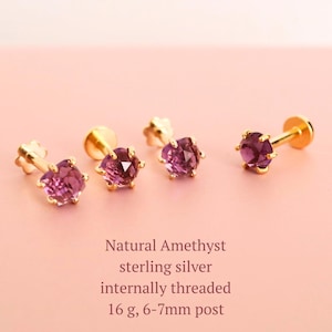 Op de afbeelding: Vier goudkleurige oorstekers met gefacetteerde, paarse amethist edelstenen. De oorbellen worden gepresenteerd op een roze achtergrond. Tekst op de afbeelding luidt "Natural Amethyst sterling silver internally threaded 16 g, 6-7mm post."