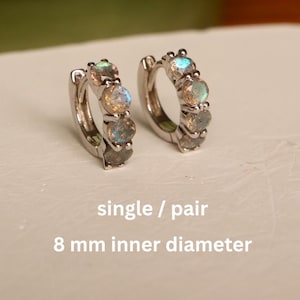 Peut inclure: Deux boucles d'oreilles créoles argentées, chacune ornée de cinq pierres précieuses irisées. Le diamètre intérieur des boucles d'oreilles est de 8 mm. Le texte de l'image indique "single / pair".