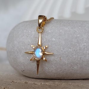 May include: A gold necklace with a moonstone pendant in the shape of a starburst. The pendant has small clear stones around the moonstone.