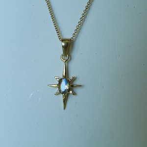 Puede incluir: Collar dorado con un colgante en forma de estrella. El colgante tiene una piedra preciosa iridiscente central y ocho puntas, cada una con un peque&ntilde;o acento transparente. La delicada cadena dorada completa esta elegante joya.