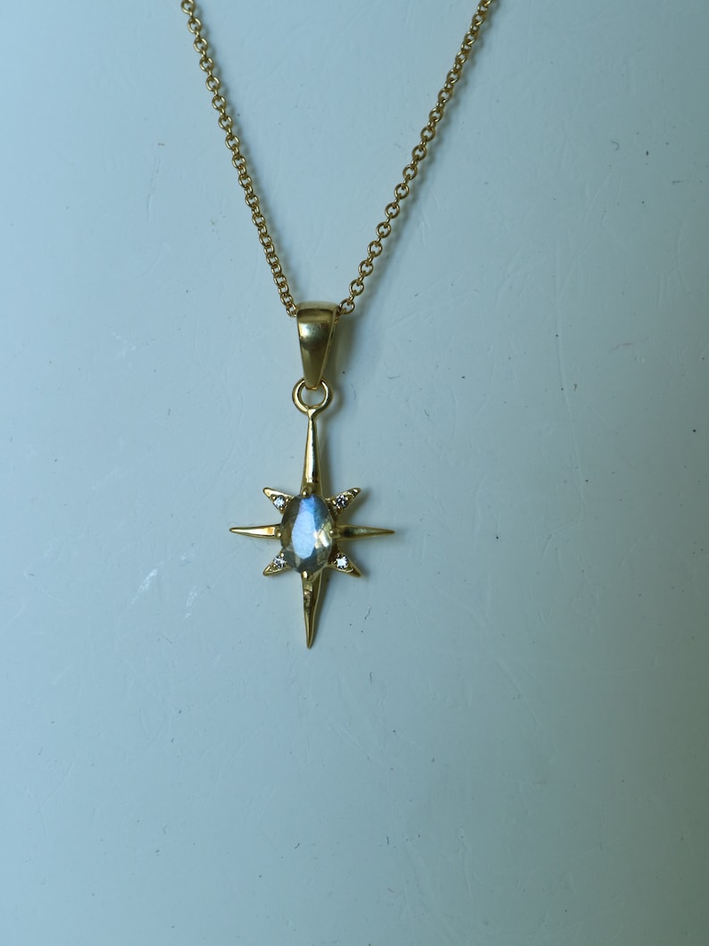 Puede incluir: Collar dorado con un colgante en forma de estrella. El colgante tiene una piedra preciosa iridiscente central y ocho puntas, cada una con un peque&ntilde;o acento transparente. La delicada cadena dorada completa esta elegante joya.