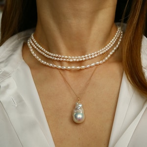 Può includere: Una collana di perle a strati con un ciondolo di perla grande e irregolare. La collana è realizzata con perle bianche e una catena d'oro.