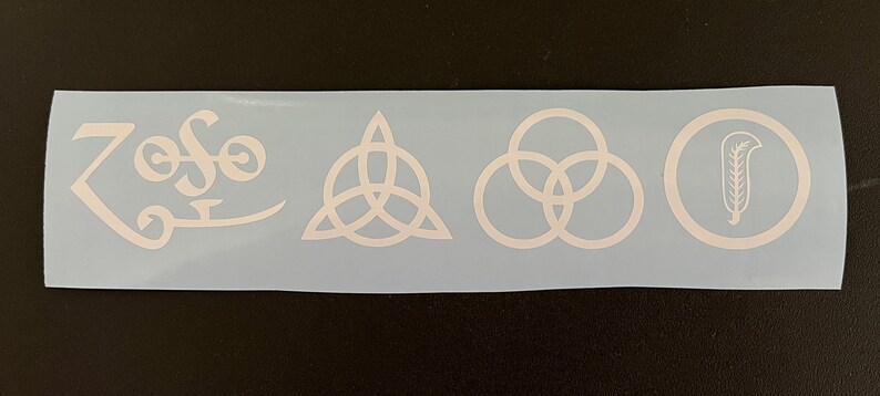 Może przedstawiać: Biała naklejka winylowa z czterema symbolami: "Zoso", tr&oacute;jkątem z k&oacute;łkiem w środku, trzema splecionymi k&oacute;łkami i k&oacute;łkiem z pi&oacute;rem w środku. Symbole te są często kojarzone z zespołem rockowym Led Zeppelin.