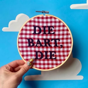 Può includere: Un cerchio di tessuto gingham rosso e bianco con il testo "DIE BART, DIE" ricamato in nero.