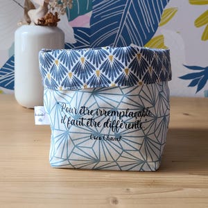 Peut inclure: Un petit panier de rangement en tissu avec un motif géométrique et floral. Le panier est bleu et blanc avec un dessus replié. Le texte "Pour être irremplaçable il faut être différente" est imprimé sur le devant.