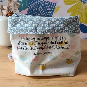 Peut inclure: Un panier de rangement en tissu avec un motif de vagues bleu et blanc sur le bord supérieur. Le corps principal présente un motif de cygnes et une citation française. Le fond a un motif floral.