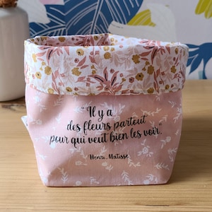 Peut inclure: Un panier en tissu rose avec un motif floral et un bord roulé. Le panier porte une citation en français : "Il y a des fleurs partout pour qui veut bien les voir." de Henri Matisse.