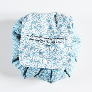 Könnte beinhalten: Eine blaue und weiße Kosmetiktasche mit geometrischem Muster und einem Zitat auf Französisch, das lautet "La beauté commence au moment où vous décidez d'être vous même." von Coco Chanel.