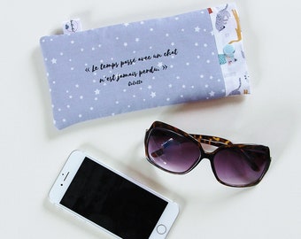 May include: A gray and white fabric eyeglass case with a quote in French that reads "Le temps passé avec un chat n'est jamais perdu."  The case is decorated with white stars and a small cat illustration. A pair of brown tortoise shell sunglasses and a white smartphone are also in the image.