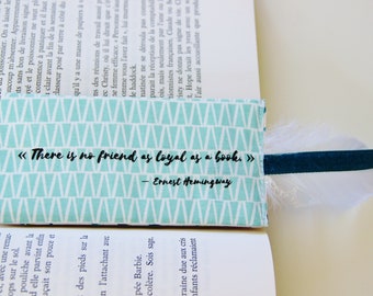 May include: A teal blue bookmark with a white triangle pattern and the quote "There is no friend as loyal as a book." by Ernest Hemingway. The bookmark has a white feather and a dark blue ribbon attached.
