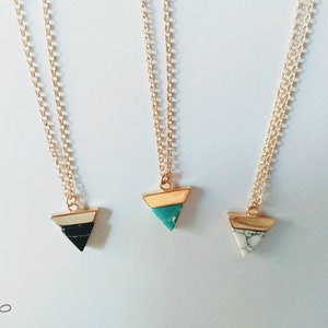 May include: Three gold chain necklaces with triangle pendants. The pendants are made of white, black, and turquoise marble with gold trim.
