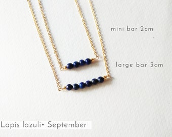 May include: Two gold necklaces with lapis lazuli beads. The top necklace has a 2 cm bar with 5 beads and the bottom necklace has a 3 cm bar with 7 beads.  Lapis lazuli is the birthstone for September.