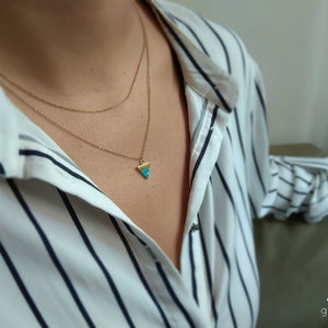 May include: A gold filled necklace with a turquoise triangle pendant. The necklace is layered on a model wearing a white and black striped shirt.
