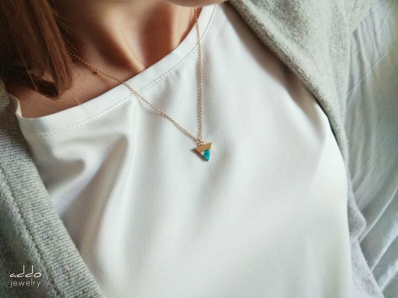 May include: A gold chain necklace with a turquoise triangle pendant.