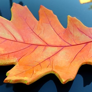 May include: A ceramic leaf dish in shades of orange and yellow, with a detailed vein pattern. The dish is shaped like an oak leaf and has a glossy finish.