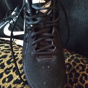 May include: Black Nike athletic shoes with white laces and a white Nike logo on the side. The shoes have a black suede toe and a black rubber sole.