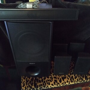 Puede incluir: Un sistema de cine en casa Sony negro con una barra de sonido, un subwoofer y cuatro altavoces sat&eacute;lite. El subwoofer tiene un gran puerto circular. Los altavoces est&aacute;n sobre una superficie con estampado de leopardo.