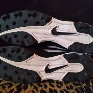 May include: Black and white baseball cleats with a Nike swoosh logo on the side. The cleats have a white midsole and a black outsole with a tread pattern.