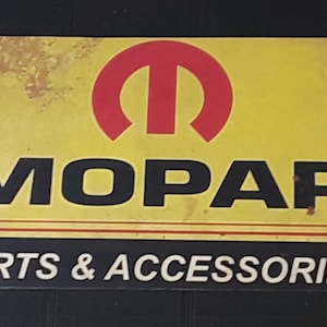 May include: A yellow and black metal sign with the Mopar logo and the text "PARTS & ACCESSORIES". The Mopar logo is a red circle with a stylized letter "M" inside.