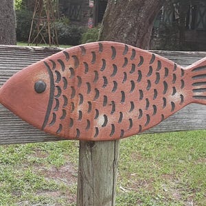 May include: A wooden fish sculpture painted orange with black details. The fish is mounted on a wooden post.
