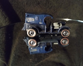 May include: A blue toy police van with a black engine and black wheels with red rims. The van has "POLICE" written on the side.