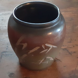 Puede incluir: Un jarrón de cerámica marrón con un esmalte marrón oscuro y diseños abstractos blancos. El jarrón tiene una boca ancha y un cuerpo redondeado.