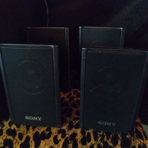 Puede incluir: Cuatro altavoces negros Sony con una parte frontal de malla, dispuestos sobre una superficie con estampado de leopardo. Los altavoces son rectangulares y tienen el logotipo de Sony en la parte inferior. El fondo es oscuro.