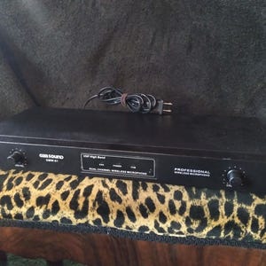 May include: A black Gem Sound GMW-01 dual channel wireless microphone receiver unit. The front panel features a power switch, two volume control knobs, and a central display area labeled VHF High Band, Dual Channel Wireless Microphone.