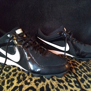 May include: A pair of black and white Nike baseball cleats with a white swoosh logo on the side.