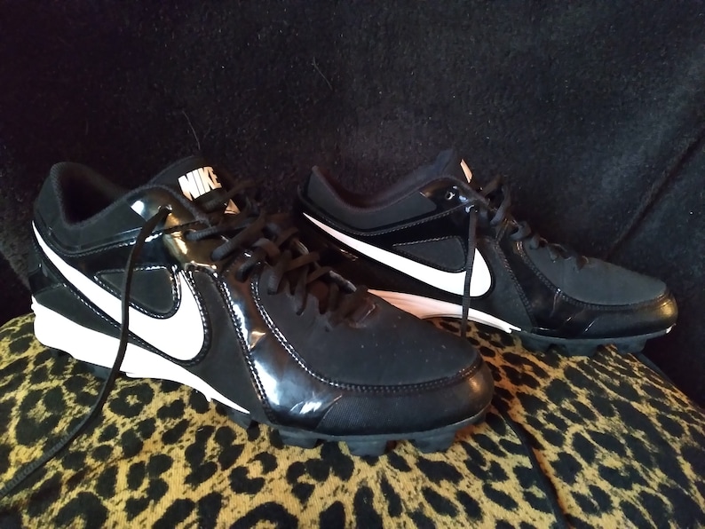 May include: A pair of black and white Nike baseball cleats with a white swoosh logo on the side.