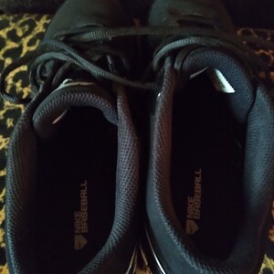 May include: A pair of black baseball cleats with white accents and the text "NIKE BASEBALL" on the inside of each shoe.