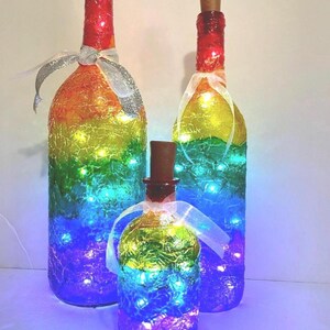 May include: Three glass bottles decorated with rainbow colors and white lights. The bottles are different sizes and have a textured surface.