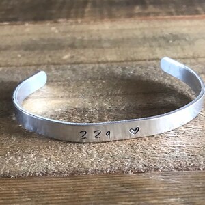 May include: A silver metal bracelet with the numbers "229" and a small heart engraved on it.