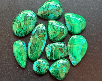 May include: A collection of polished malachite gemstones in various shapes, including oval, teardrop, and round. The stones display vibrant green hues with intricate swirling patterns and some areas of blue-green. The gemstones are arranged on a dark surface.