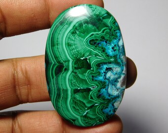 May include: Oval cabochon gemstone with green, blue, and white swirling patterns. The stone has a smooth, polished surface.