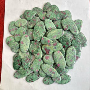 May include: A collection of green and red gemstone cabochons. The stones are oval and teardrop shaped and have a speckled pattern.