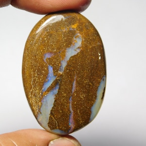 May include: A brown oval opal cabochon with blue and white iridescent flashes. The opal has a rough, textured surface.