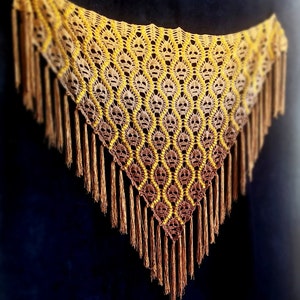 May include: A crocheted shawl with a skull pattern in shades of brown and yellow. The shawl has a fringe border.