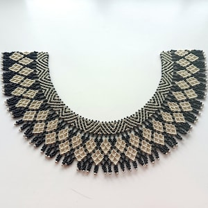 Puede incluir: Un collar de cuentas negras y plateadas con un patrón geométrico. El collar tiene forma de collar y tiene una franja en la parte inferior.