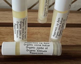 May include: A close-up of six white tubes of peppermint lip balm. The tubes are labelled with the ingredients: organic cocoa butter, organic jojoba oil, organic beeswax, and peppermint.