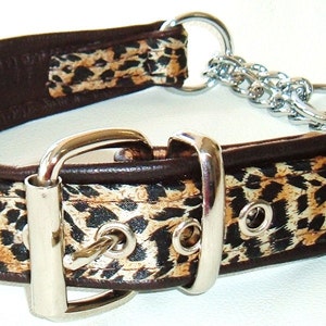 May include: A dog collar featuring a brown leather backing and a leopard print fabric overlay. It has a silver-coloured metal buckle and a chain for leash attachment. The collar is designed for medium to large dogs.
