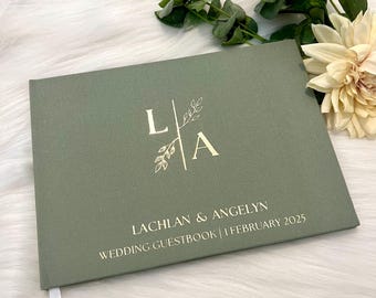 Könnte beinhalten: Salbeigrünes Hochzeitsgästebuch mit goldfarbenem Folienschriftzug. Das Cover zeigt die Initialen "L A" mit floralem Design, die Namen "Lachlan & Angelyn" und das Datum "1. Februar 2025". Ein weißes Leseband ist sichtbar.