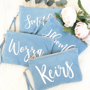 May include: Four denim zippered pouches with white cursive lettering. The pouches are stacked on top of each other. The lettering reads "Smith", "Brown", "Wozra", and "Keirs".