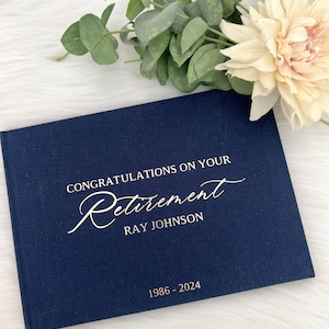 Op de afbeelding: Een donkerblauw linnen gastenboek met gouden letters met de tekst "Gefeliciteerd met uw pensioen Ray Johnson 1986 - 2024".