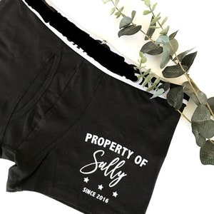 May include: Black boxer shorts with a white elastic waistband and white text that reads "PROPERTY OF Sally SINCE 2016".