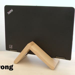 K&ouml;nnte beinhalten: Ein schwarzer Laptop mit dem ThinkPad-Logo auf dem Deckel liegt auf einem Holzst&auml;nder. Der St&auml;nder besteht aus zwei V-f&ouml;rmigen Holzst&uuml;cken. Der Laptop steht auf einer hellen Holzoberfl&auml;che. Das Wort "Strong" ist in schwarzen Buchstaben auf der Oberfl&auml;che geschrieben.