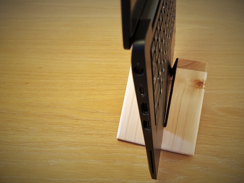 K&ouml;nnte beinhalten: Ein schwarzer Laptop steht auf einem Holzst&auml;nder. Der Laptop ist geschlossen und der St&auml;nder ist aus Naturholz.
