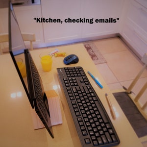 K&ouml;nnte beinhalten: Ein schwarzer Laptop ist auf einem Holztisch mit einer Tastatur, einer Maus und einem Glas Orangensaft ge&ouml;ffnet. Der Laptop ist auf einem Holzst&auml;nder aufgestellt. Der Text "K&uuml;che, E-Mails checken" ist &uuml;ber dem Laptop sichtbar.