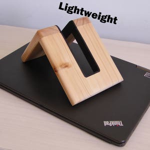 K&ouml;nnte beinhalten: Ein Laptop-St&auml;nder aus Holz mit einem schwarzen Einsatz. Der St&auml;nder ist leicht und hat ein schlichtes Design. Der St&auml;nder steht auf einem schwarzen Laptop mit dem Schriftzug "ThinkPad" auf der Unterseite.